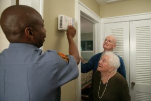 Firefighter showing elderly couple how to change batteries in detector